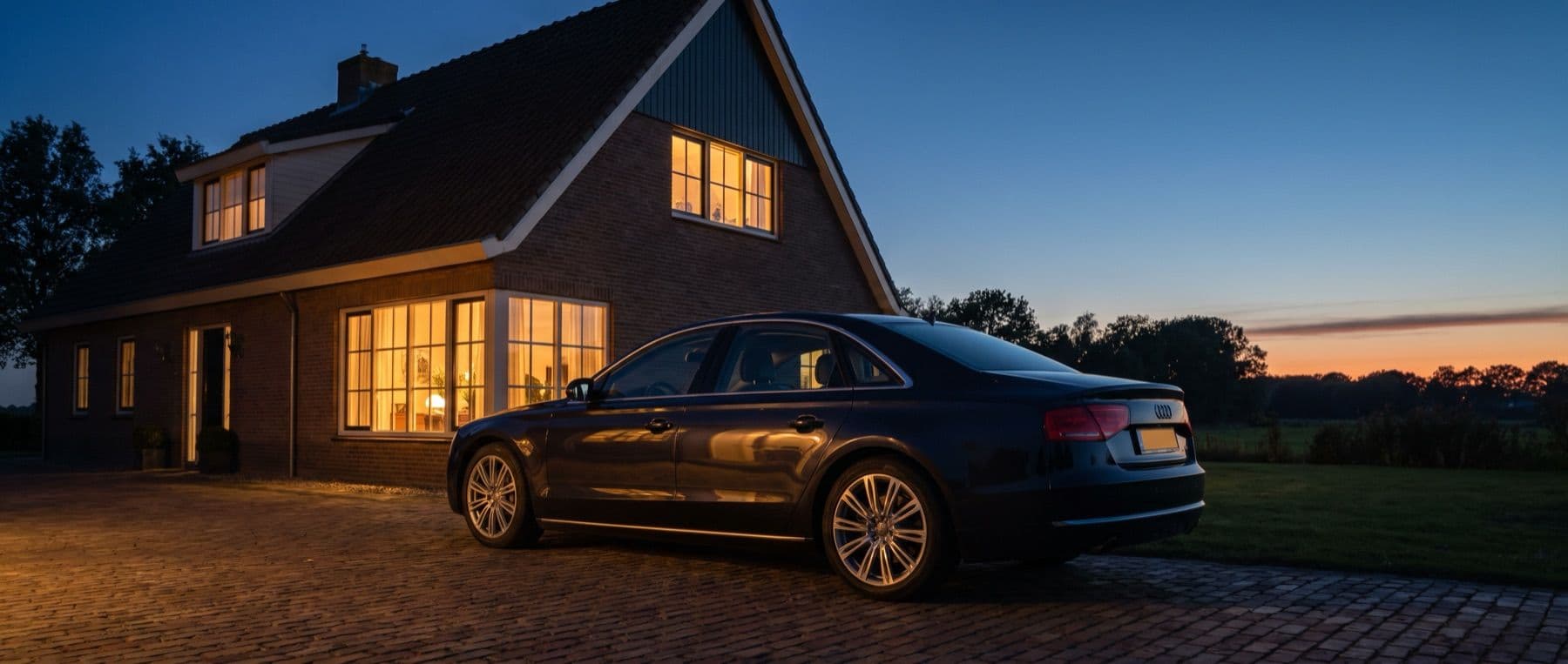 Geïmporteerde auto op de oprit bij een verlicht huis in de schemering